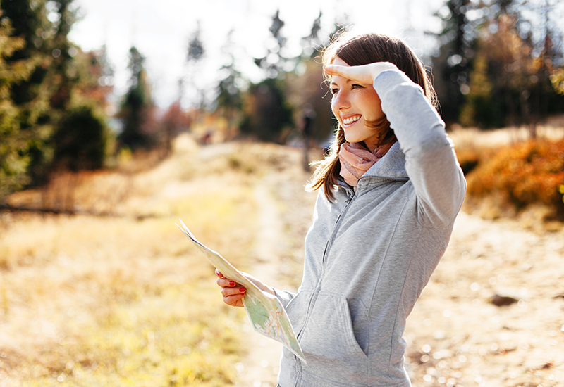 Woman in zipped up sweater and scraf holding a map and looking at paths at a trail