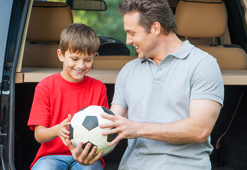 Father and son in the tialgate of their SUV holding a soccer ball