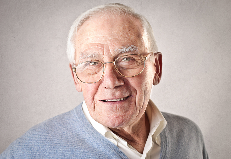 Older man in glasses in a gray sweater over a white button down shirt